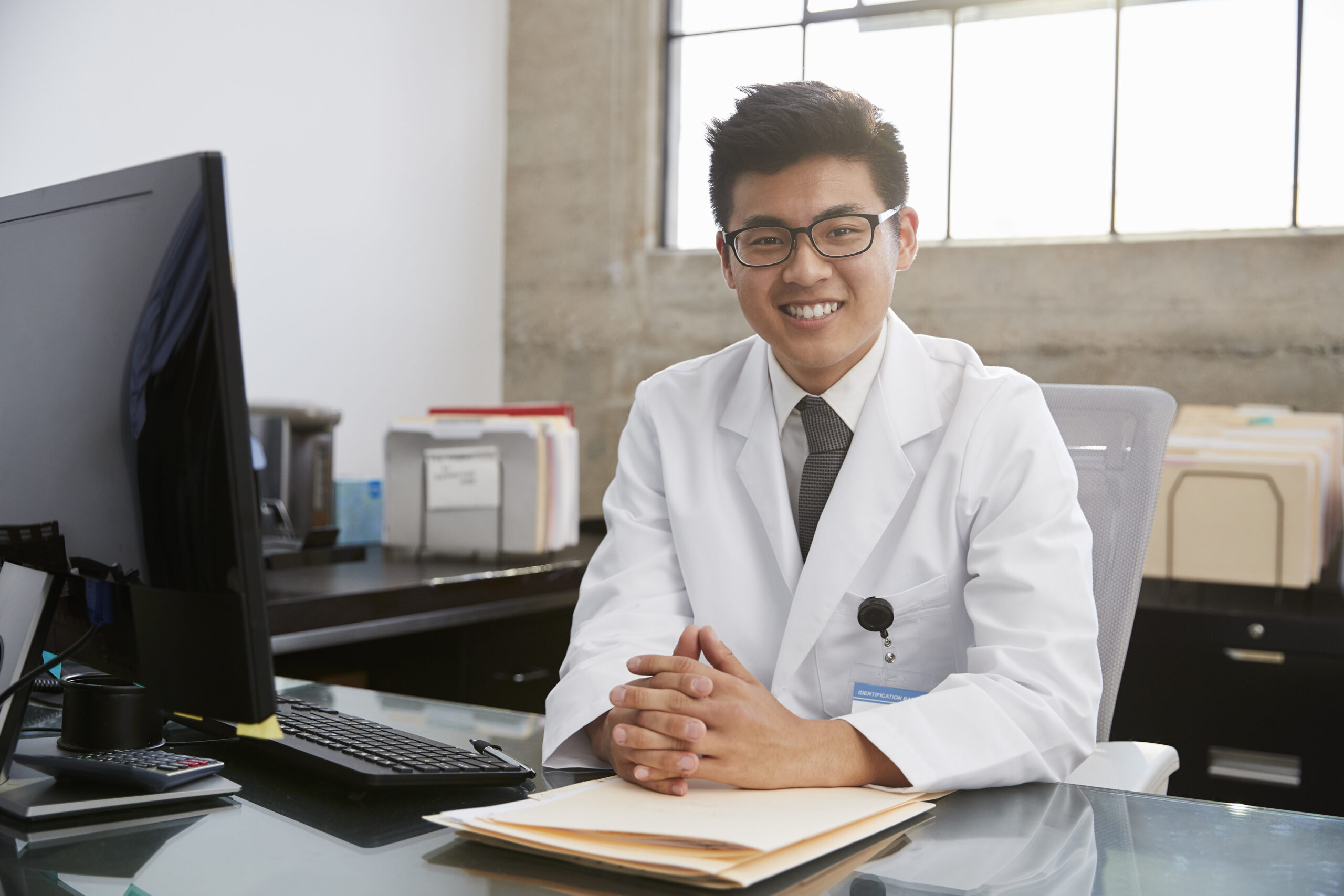 Young Asian male doctor sitting at desk, portrait Young Asian male doctor sitting at desk, portrait